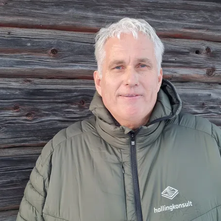 Portrett av en mann med krøllete, grått hår, iført en hvit skjorte med en mørkegrå genser over.