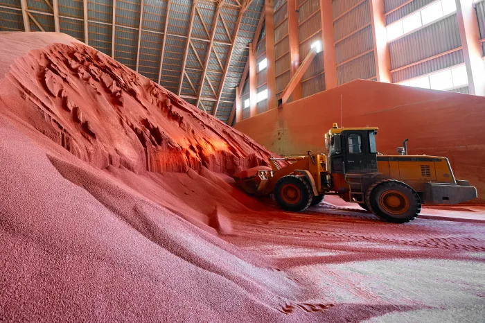 En gul traktor laster en haug med pellets i et lagerbygg.