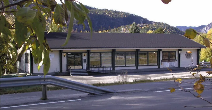 Flå IT senter sine lokaler i Flå, med en vei og autovern i forgrunnen. I bakgrunnen er det et fjell-landskap med grønn skog. Det er solskinn og lys himmel.